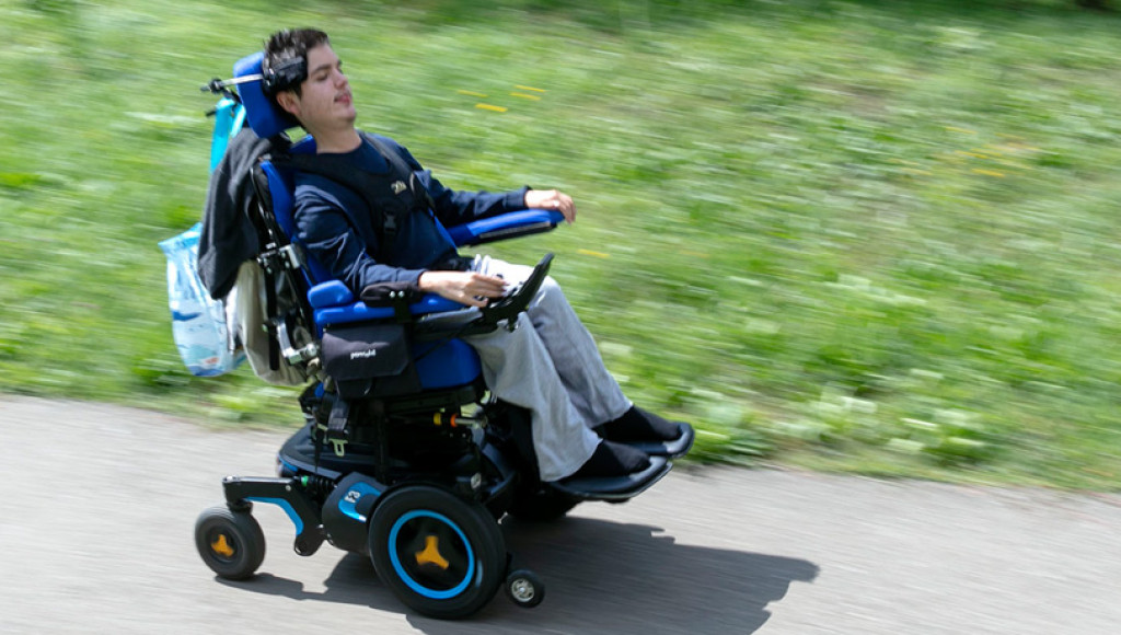 Ein Mann mit Muskelkrankheit fährt im Rollstuhl einen Weg entlang.