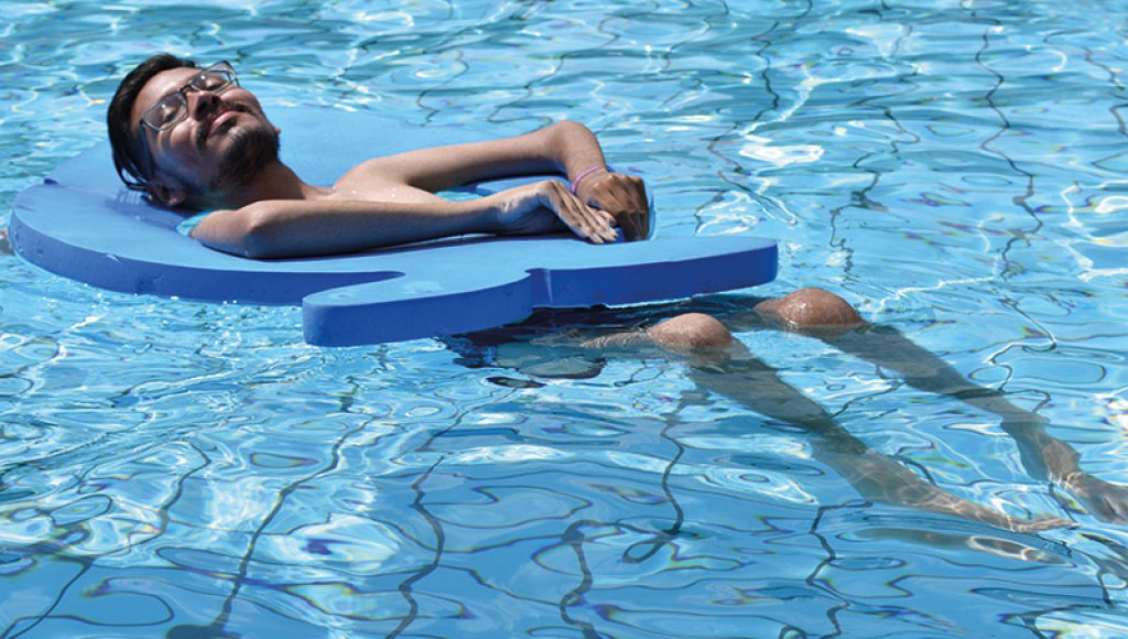Mann mit Muskelkrankheit treibt mit Schwimmhilfe entspannt im Swimming-Pool.